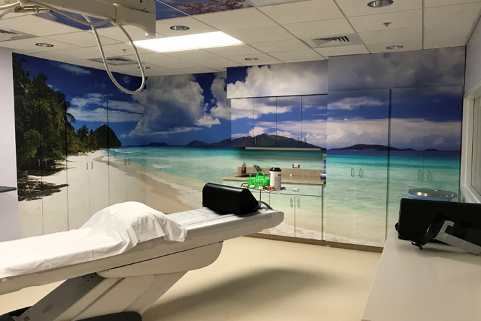 A room with a CT machine, wallpapered with a scene of a tropical beach