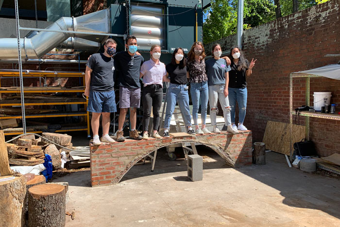 Seven architecture students standing side-by-side on a brick and tile arch they constructed