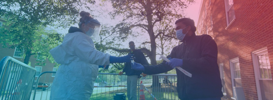 An employee in full-coverage PPE hands a sampling vial to a scientist wearing latex gloves and a face mask.