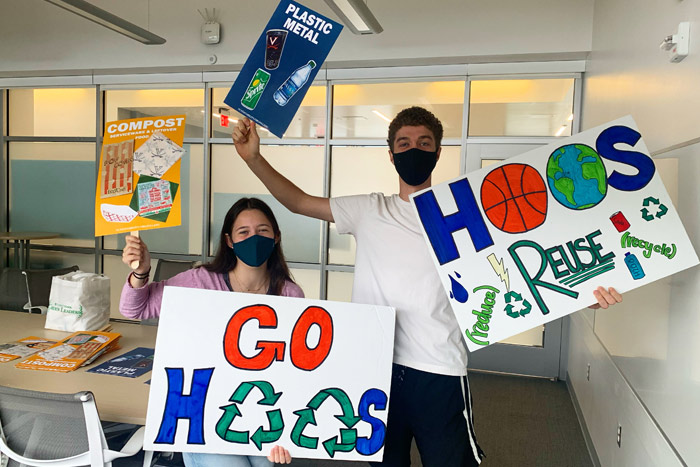 Two students hold up signs promoting composting, recycling and Hoos ReUse