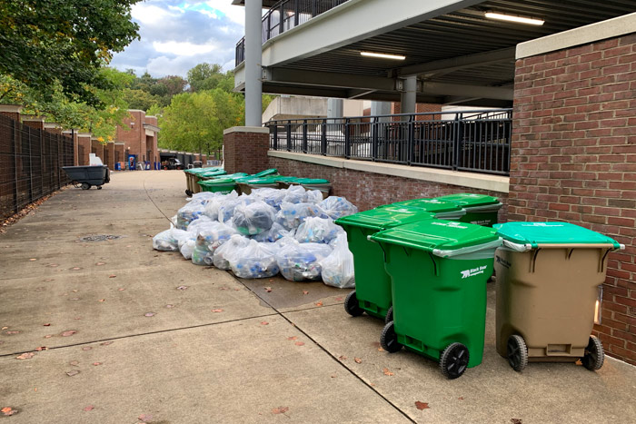 Several green waste bins and dozens of garbage bags piled along the walkway next to Scott Stadium