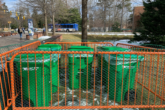 Several green waste bins fenced in by orange road barriers