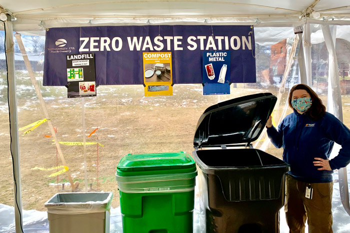 A student holds a trash bin open at a Zero Waste Station