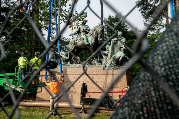 Photo through a chain-link fence of the George Rogers statue being removed by crane