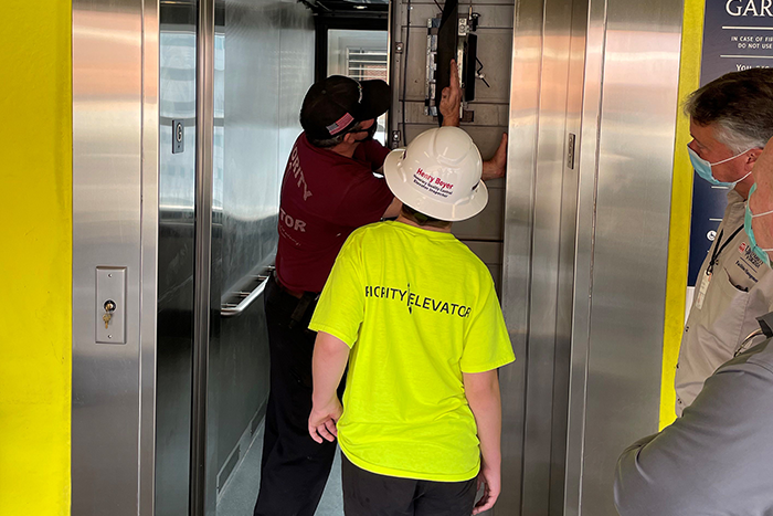 Staff member opens elevator to show teen wearing hardhat