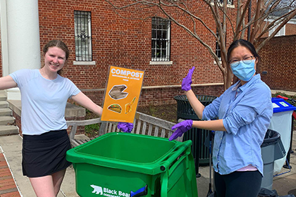 Two volunteers pose by a composting bin